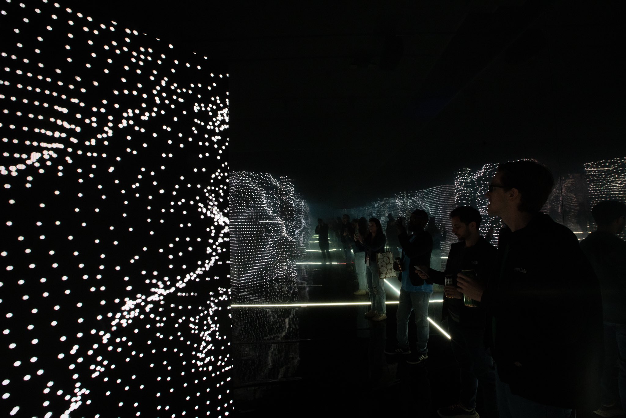interactive art installation, dark infinity mirror room with multiple people walking around