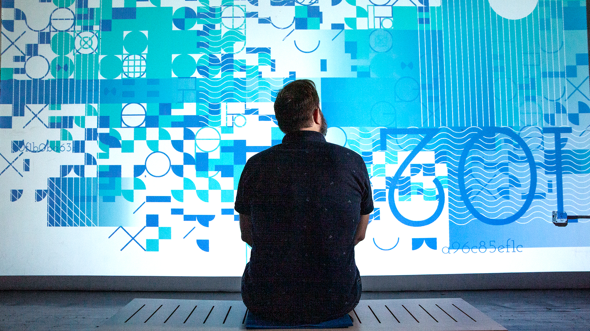 a man sits on butchain bench and watches his unqiue blockchain art generate on the screen in front of him