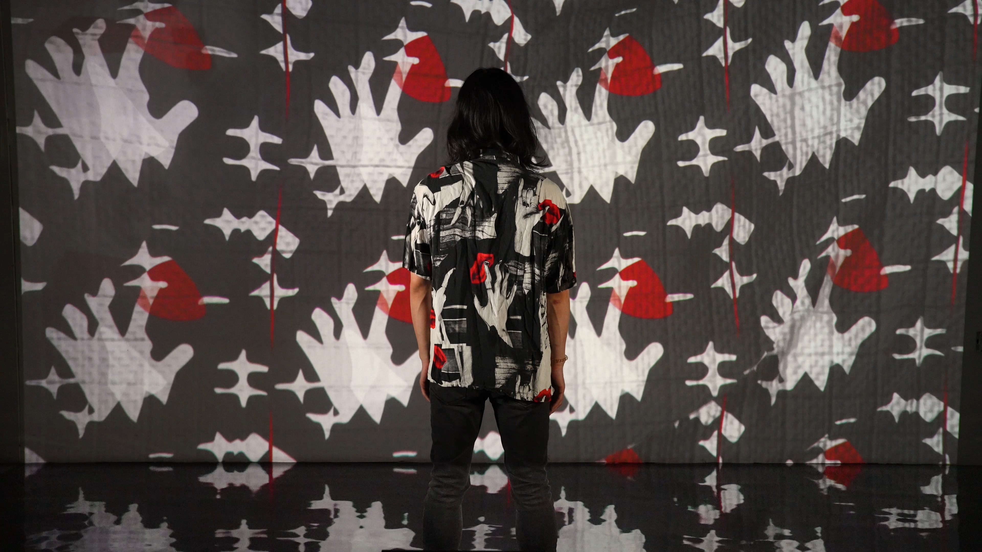 A person in the center of the image is wearing a shirt with a black, white and red pattern. The projection screen in front of the person displays a similar pattern which was generated by stable diffusion, a generative AI.
