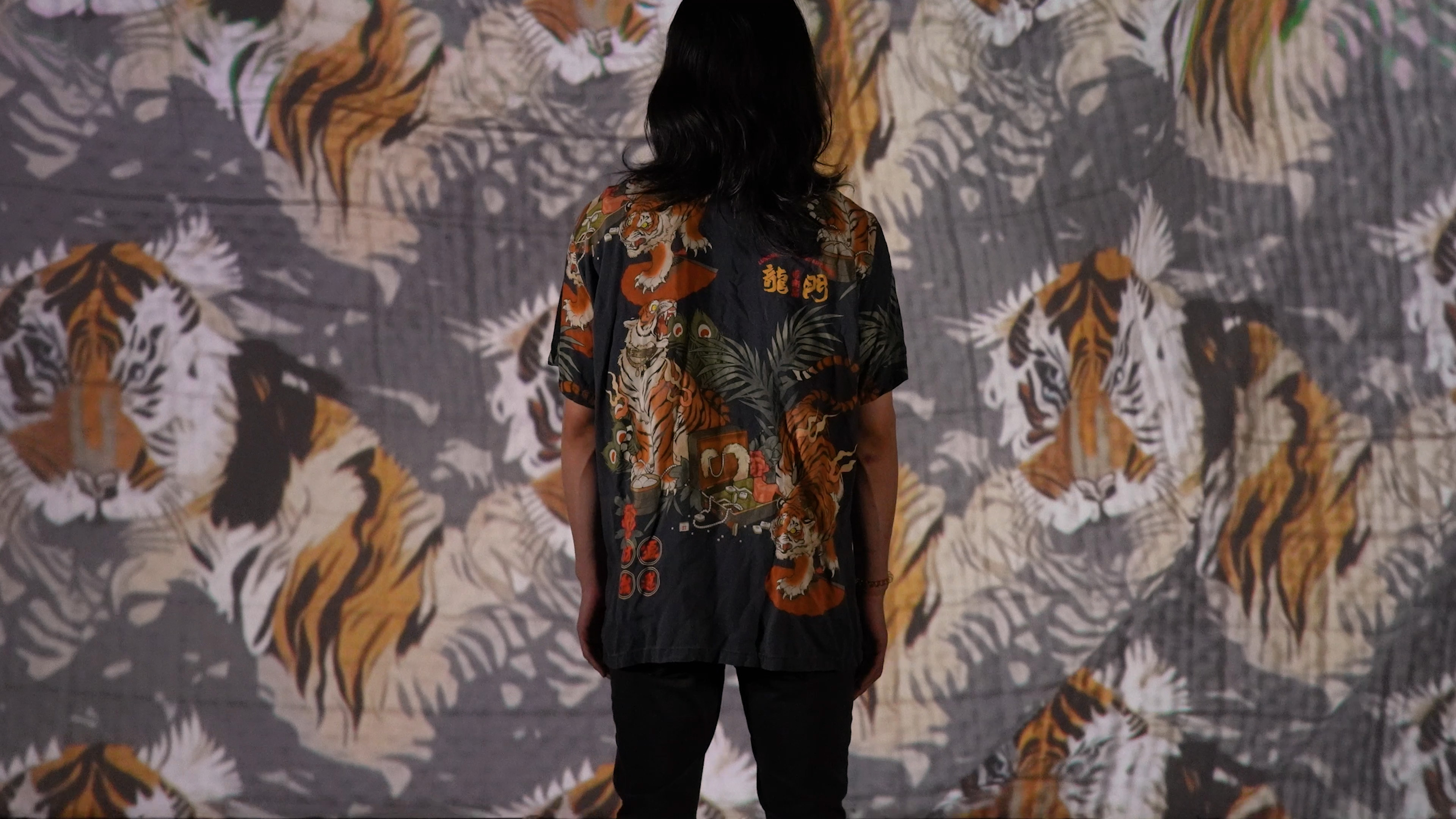 A person in the center of the image is wearing a shirt that includes tigers and palm trees. The projection screen in front of the person displays a similar pattern which was generated by the AI system.