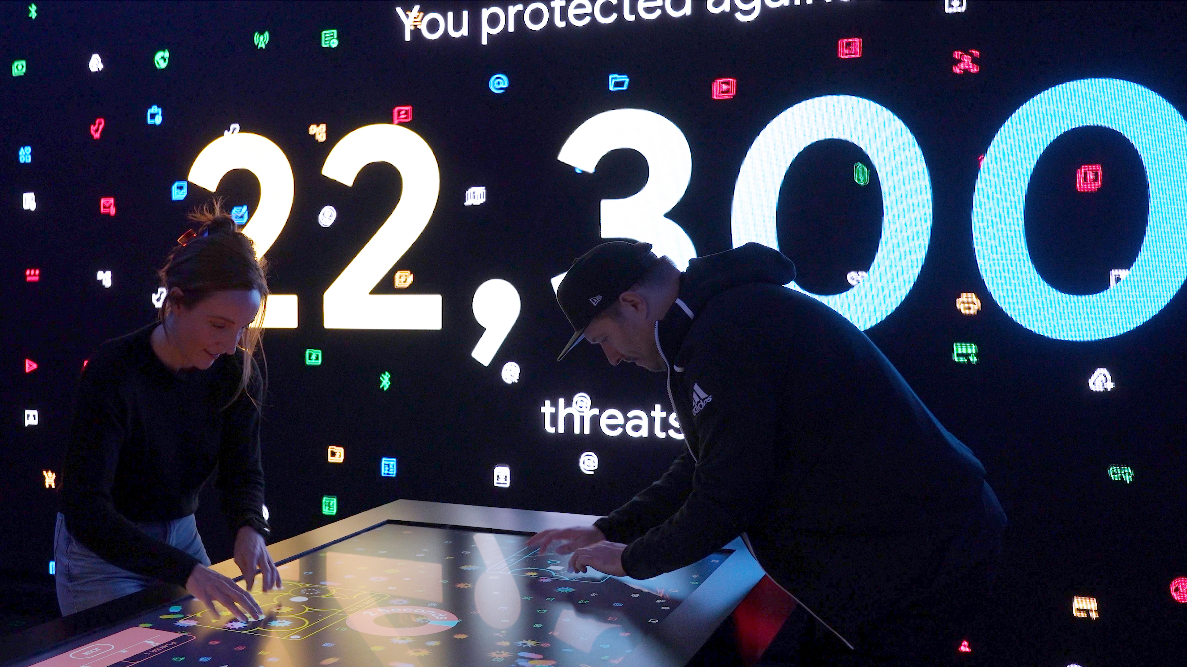 Two attendees playing the Data Defense game highly concentrated with the apparent goal to beat the high score.