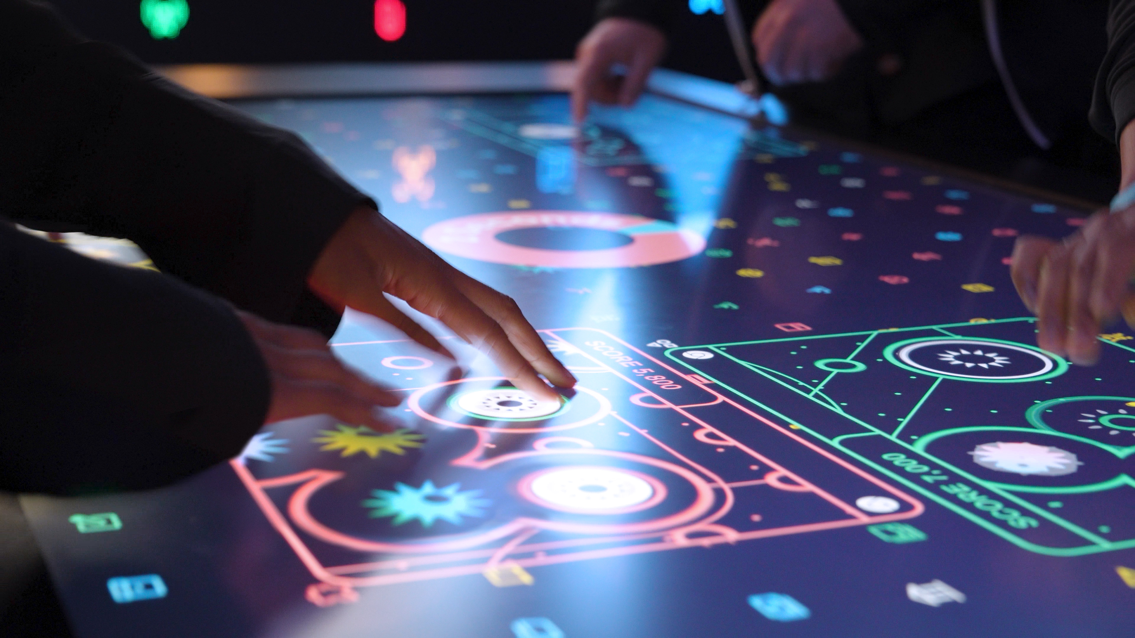 A close up of Bloomberg Technology Summit attendees hands, playing the colorful Data Defense Game on a touchtable. The display shows stylized Google Chrome windows with files being scanned for threats.