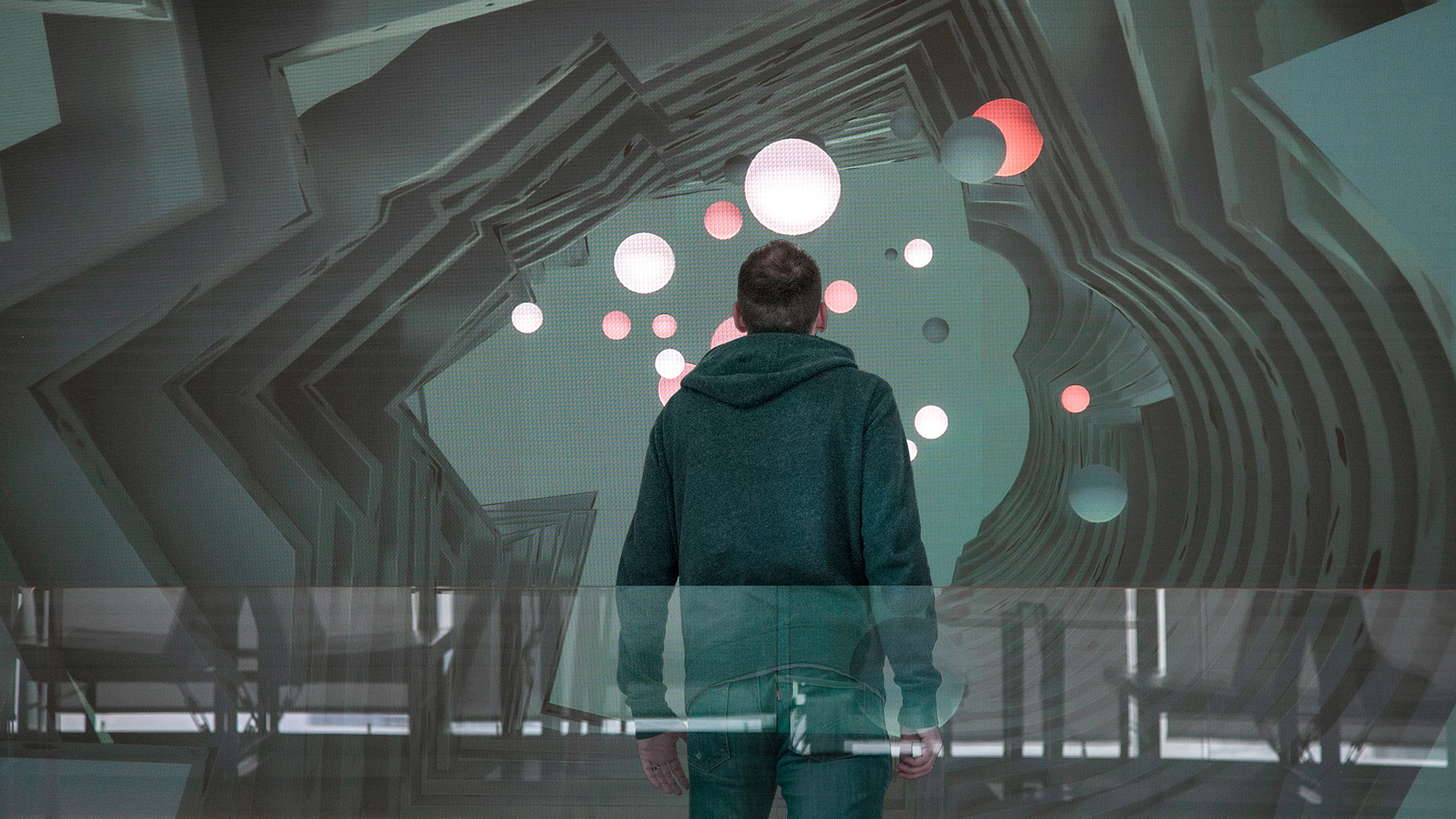 A man standing in front of a large screen within a stylish lobby. The screen displays the day version of the digital art sculpture called Day by Red Paper Heart.