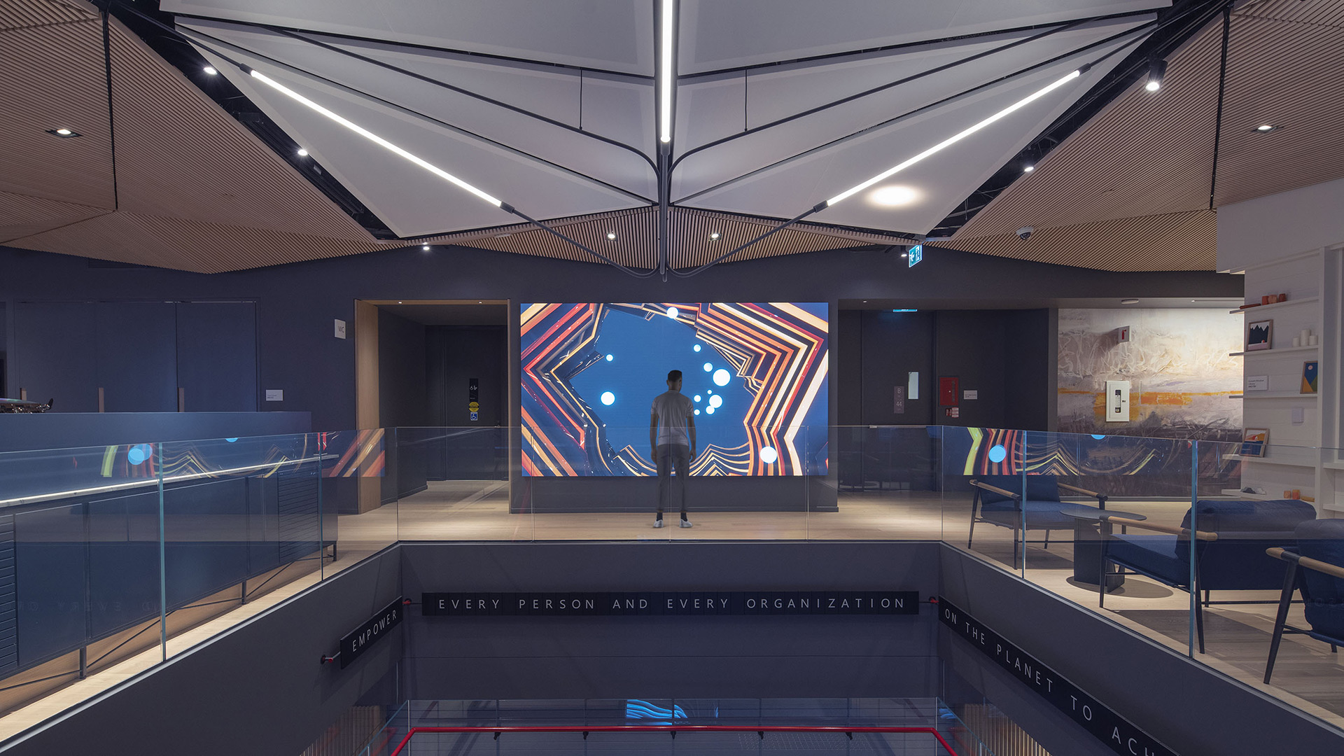 A stylish new lobby with a large screen on the wall and a person standing in front of it. The screen displays the night version of the interactive data visualization called Day by Red Paper Heart.