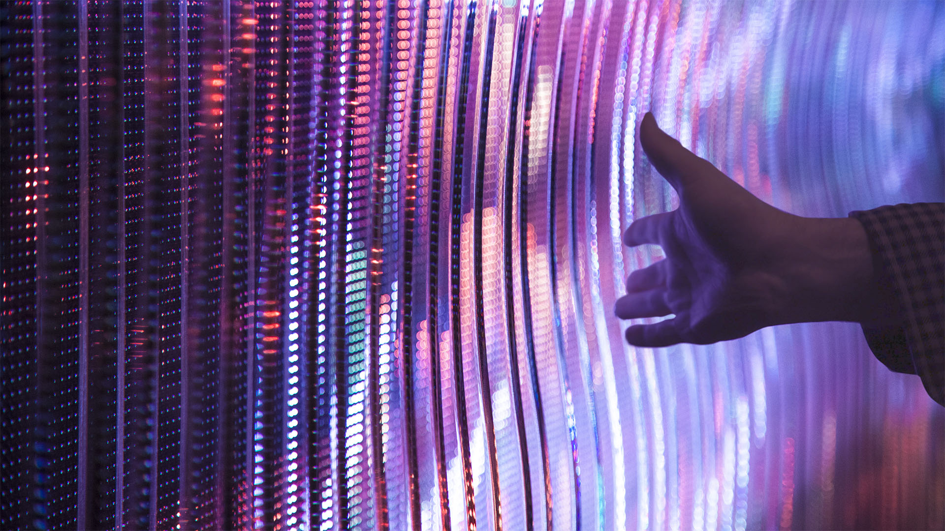 The Expression Wall, an interactive art installation, features an LED screen, a touch-sensitive plane, and custom acrylic panels. The image captures a hand making contact with the panels, sparking the creation of vibrant graphics.