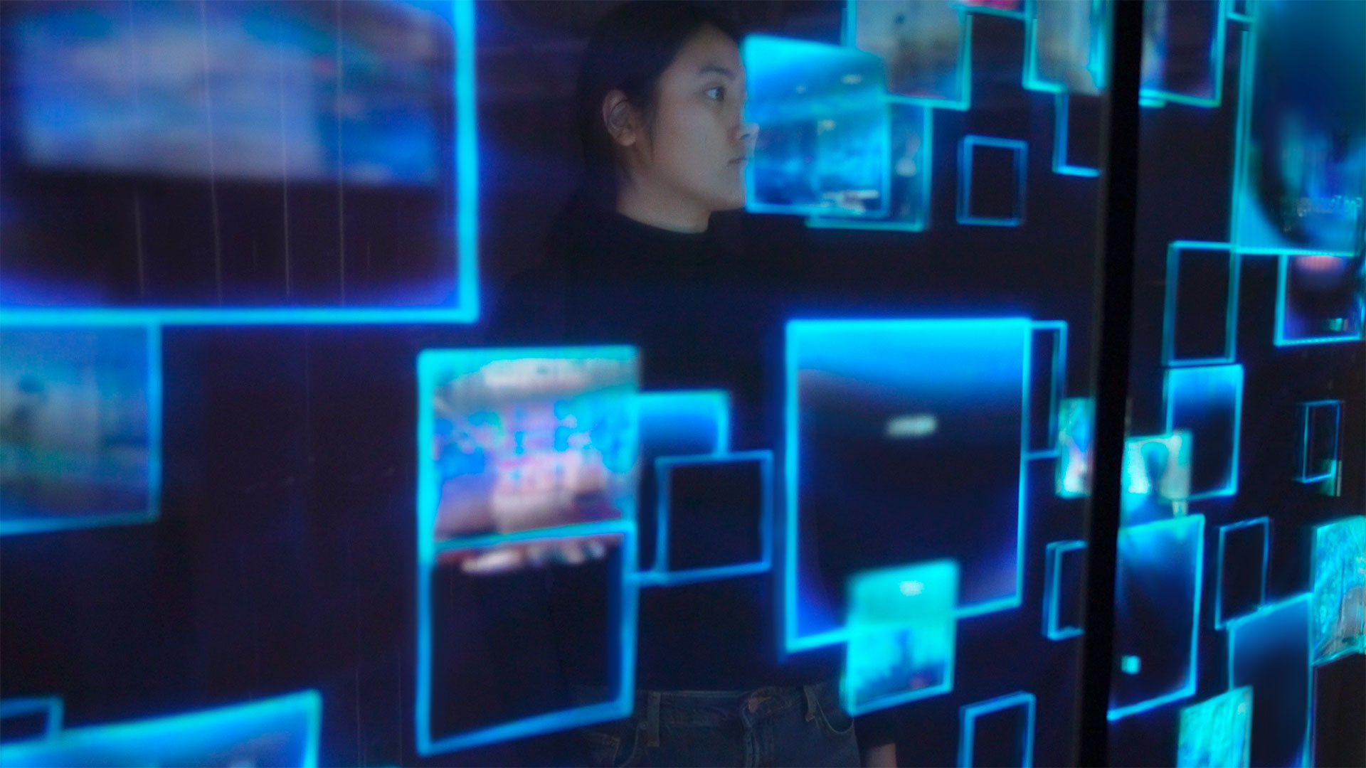 a dark room with a large interactive transparent led screen with woman interacting. photographed through the transparent touchscreen
