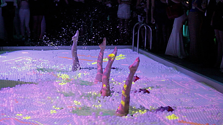 Legs up - Aqualillies perform a water ballet in a pool covered with ping pong balls and interactive projections