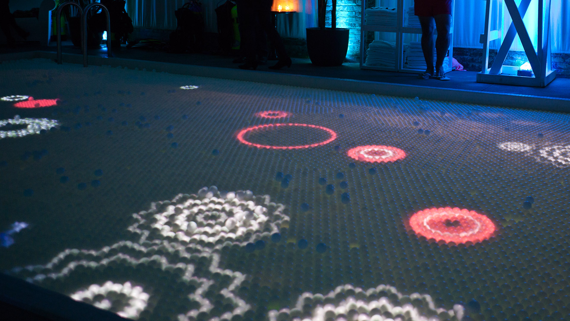 Computer generated audio reactive visuals projected on a pool covered in ping pong balls