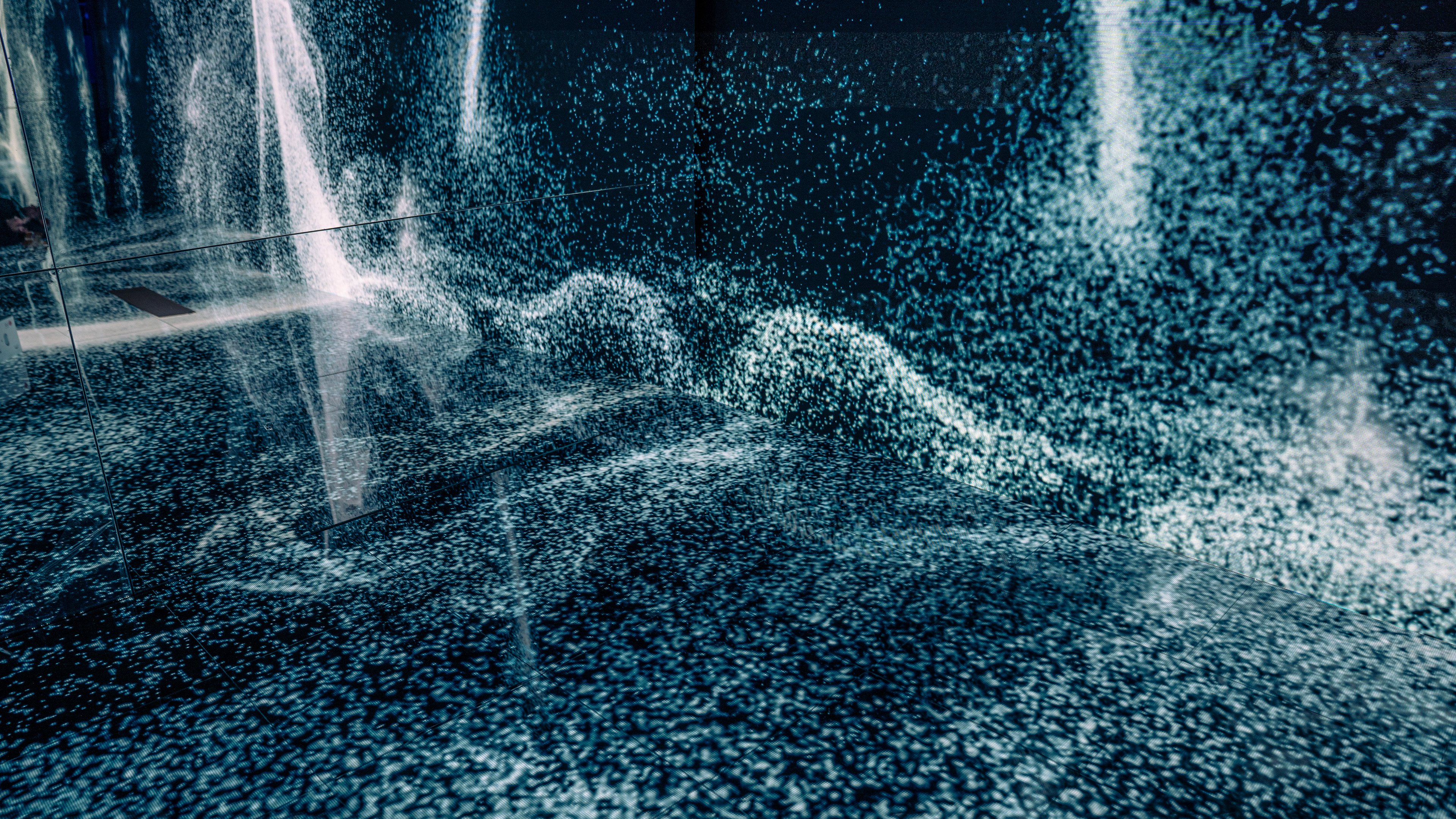 A photo of steam particle system animations playing across the walls and floors of an interactive installation. Mirrors reflect the walls and create an infinity room