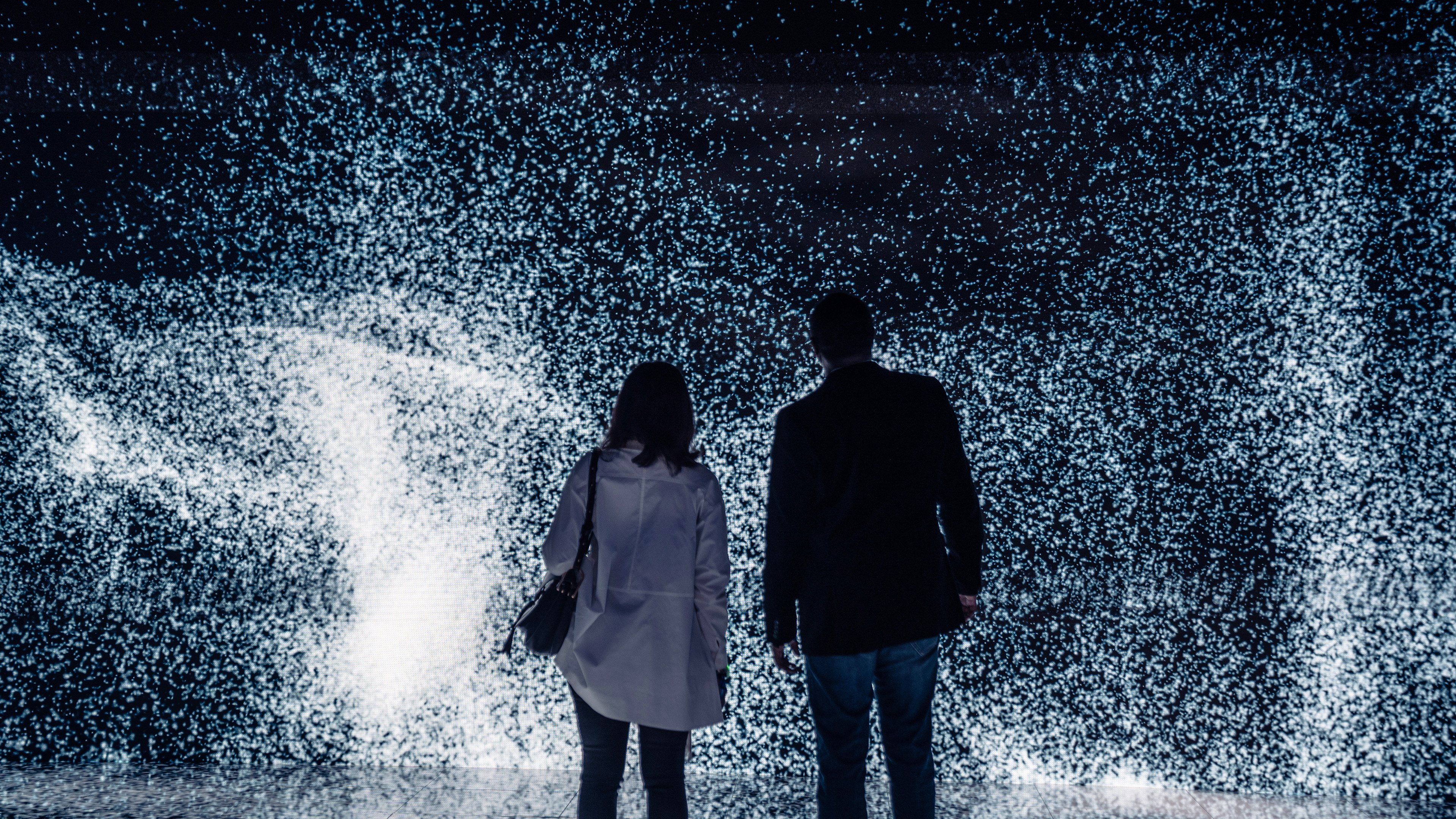 Two people standing in front of a large led wall with steam particles animating in front of them