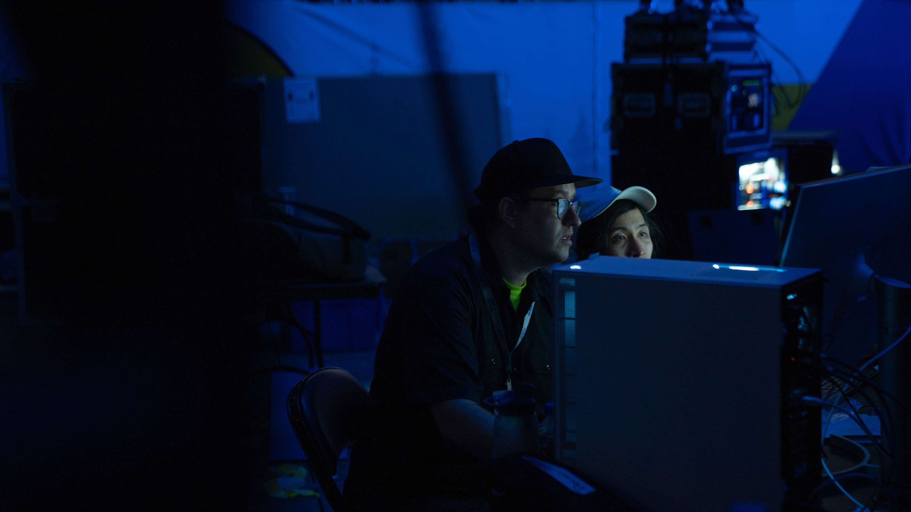 Two developers wearing hats sit and work on computers together, lit by very blue lights. They look like cool dudes