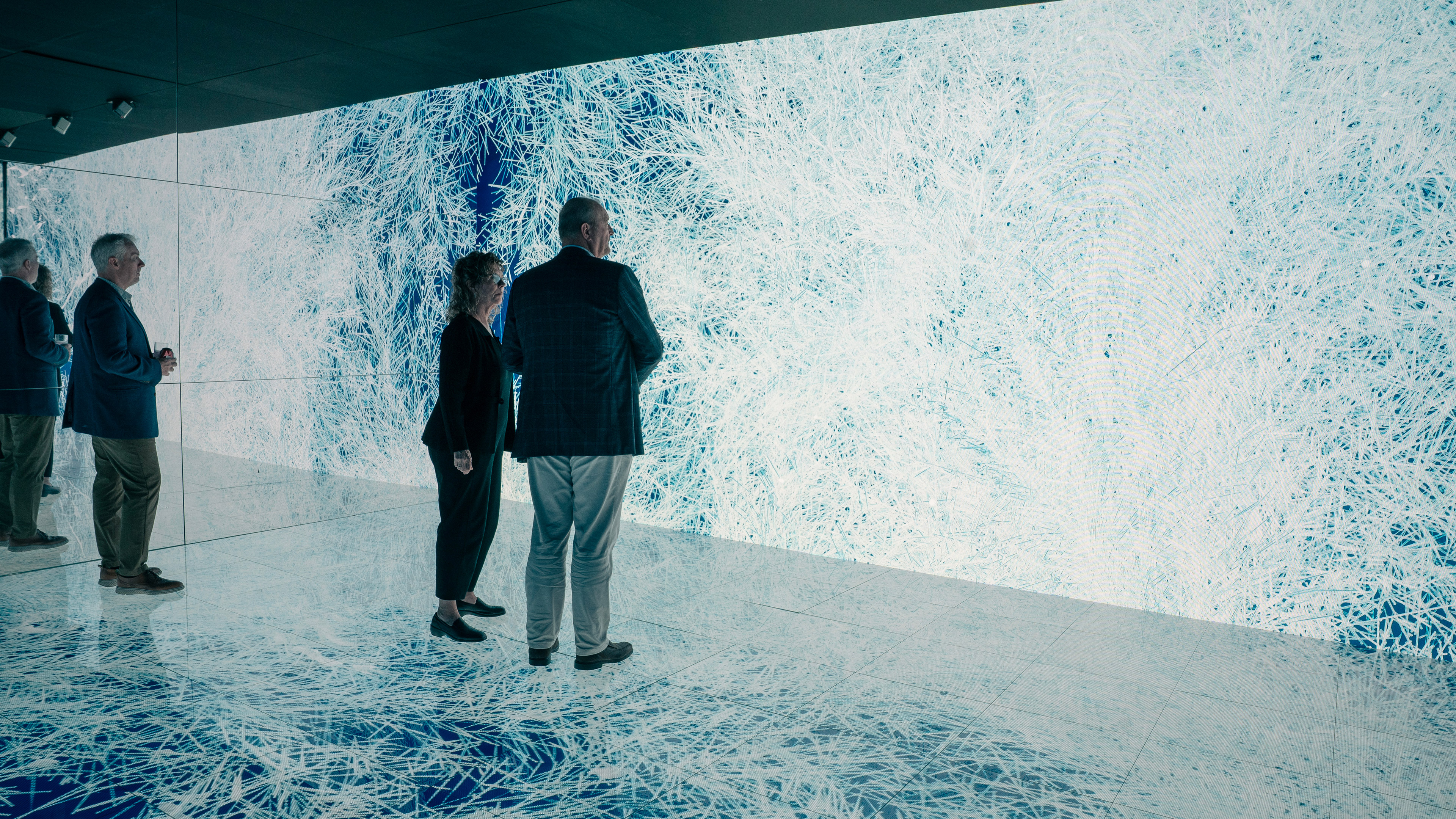 Three people standing in an interactive installation with led walls and floors. The led screens are covered with ice patterns
