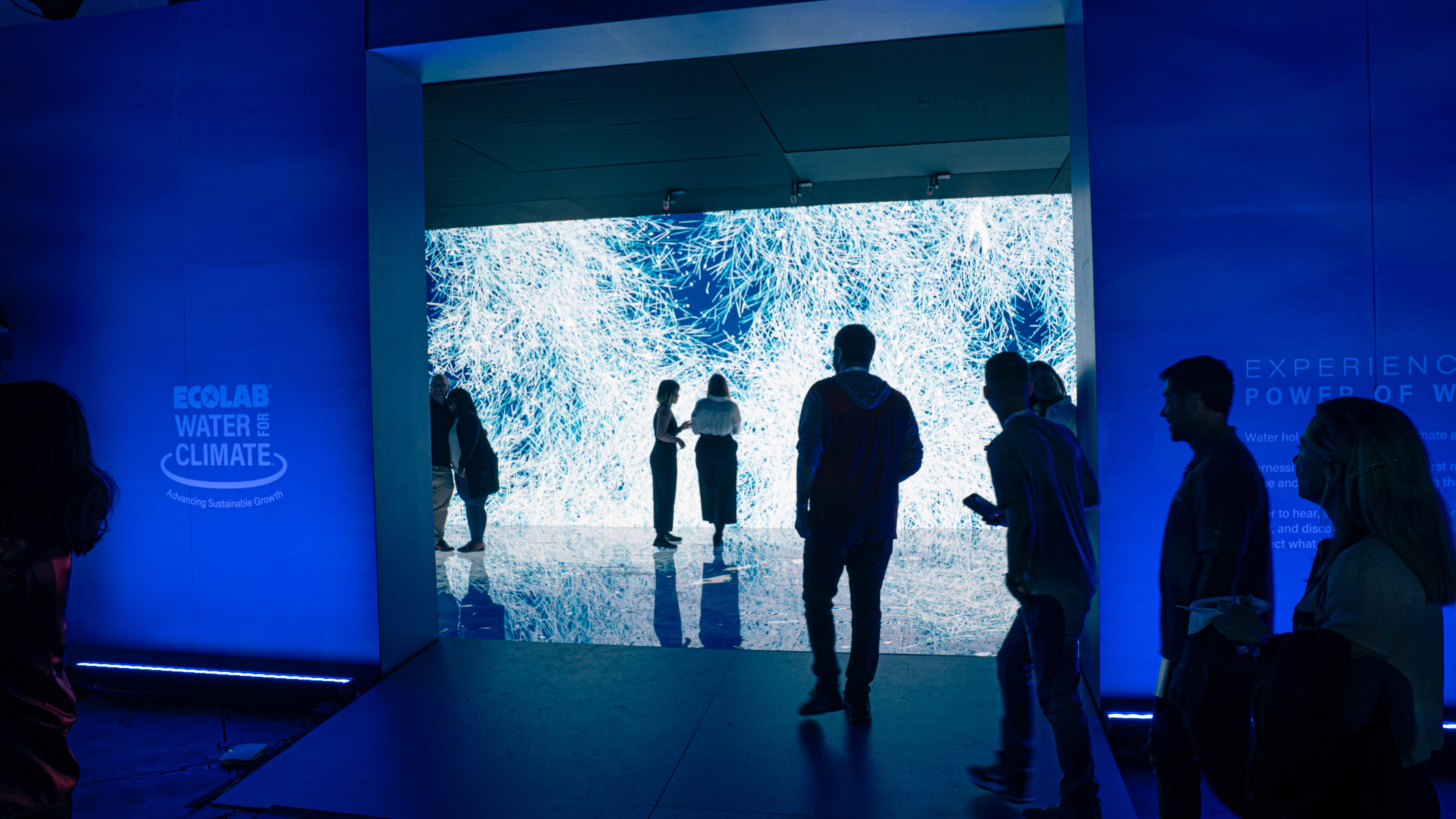 The entrance to an interactive installation with many people walking around inside and out. Ice crystals fill the screens inside the room