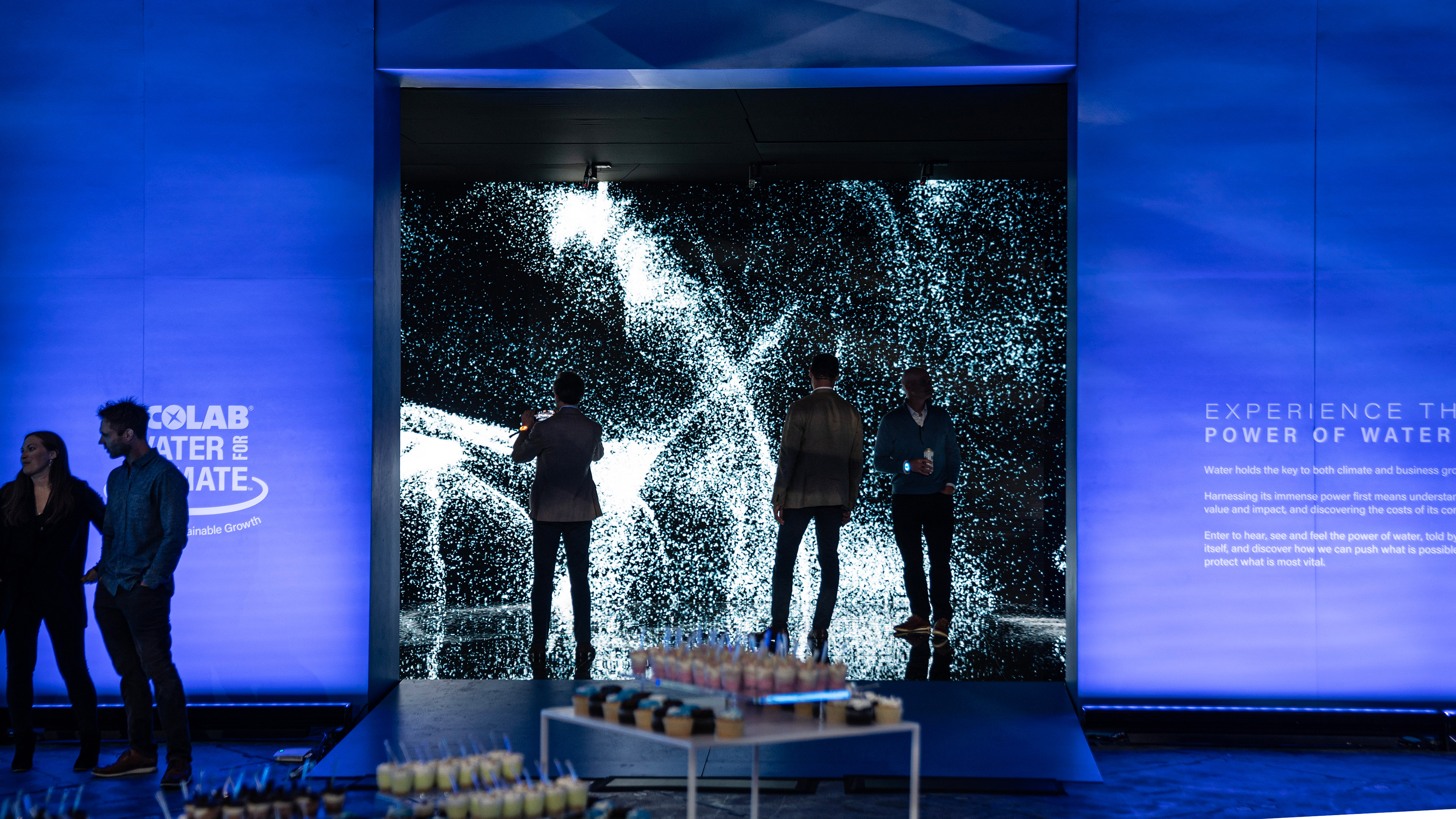 A view from outside an interactive installation with several people inside. wispy dynamic steam animations surround the visitors. Delicious cupcakes and treats can be seen in the foreground