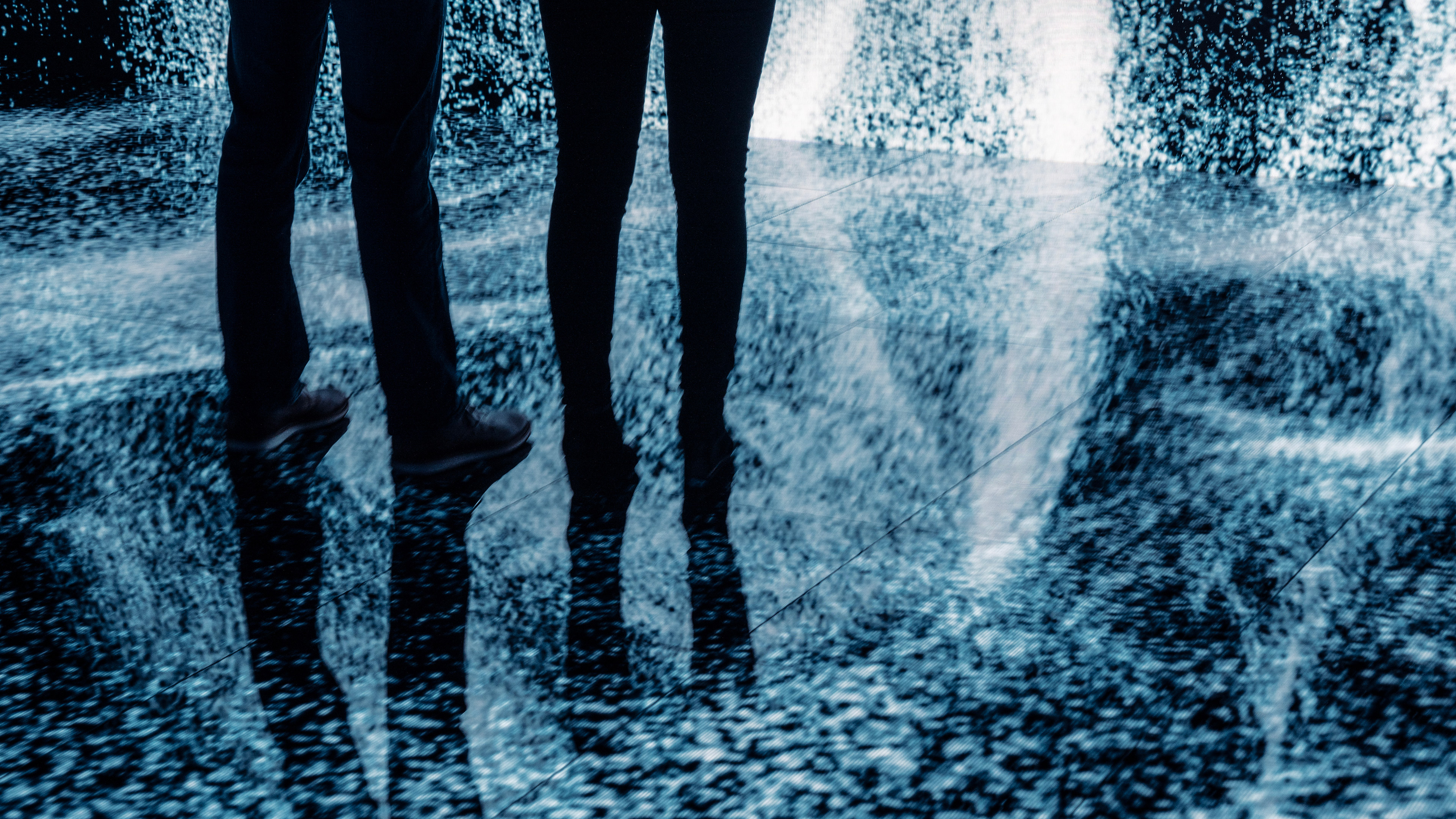 A photo of two people standing on an led floor covered with generative steamy particles