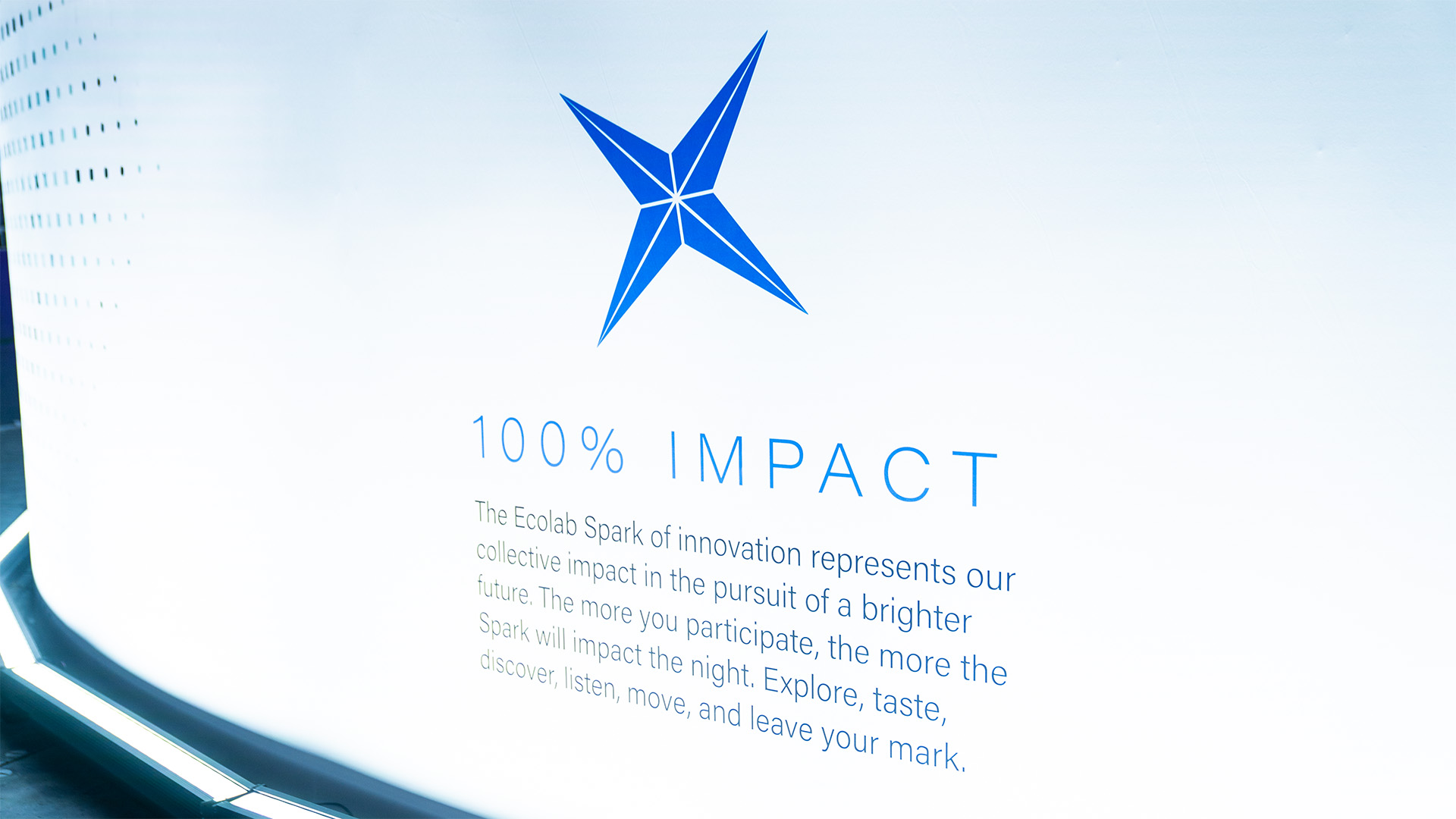 A white wall with the Ecolab logo in the center, a header text of "100% IMPACT" below, and other promotional text following after