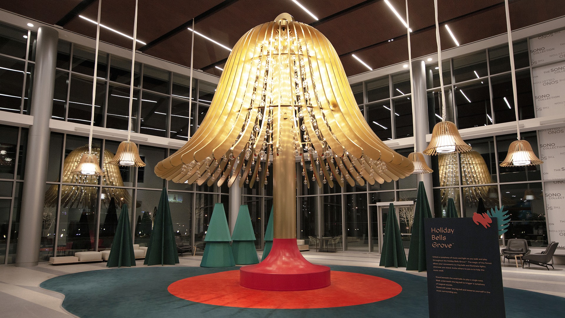 Wide shot of the Holiday Bell Grove located in the Magnificent Room at the SoNo Mall in Norwalk Connecticut. One large central bell with reactive light bulbs dangling from each arm. Six gold mini bells hang around the central bell.