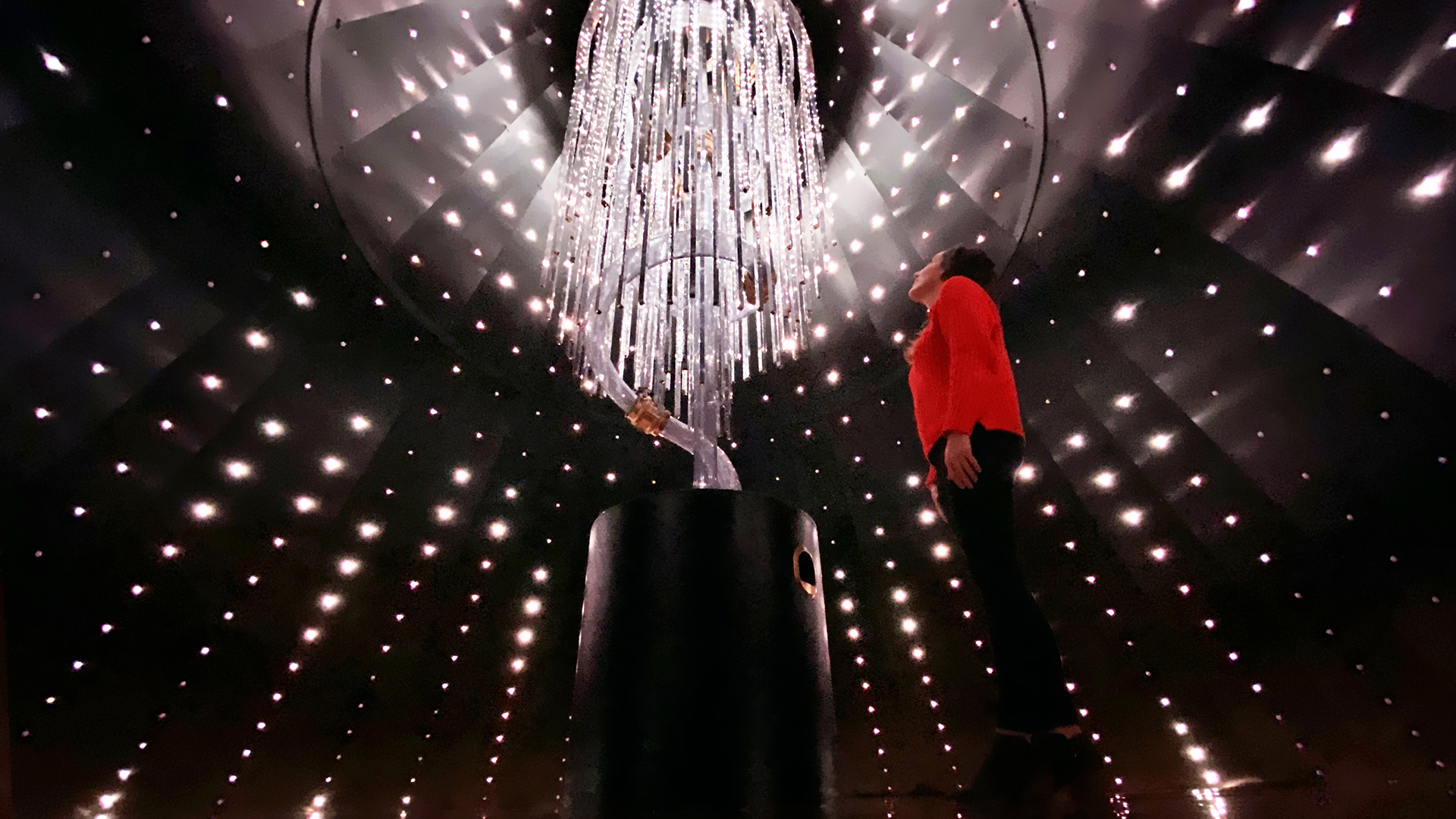 Girl is standing inside a interactive Christmas tree starting up at an LED chandelier wrapped around a pneumatic tube waiting for the LEDs that wrap around the interior walls to light up