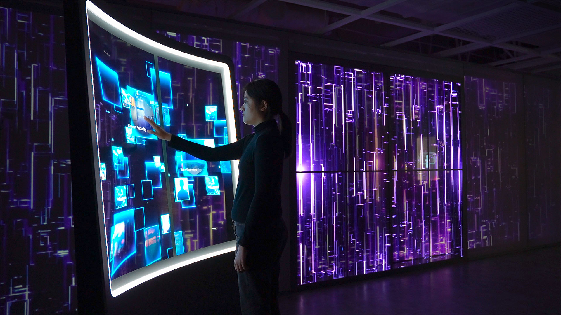 a dark room with a large interactive transparent led screen with woman interacting.